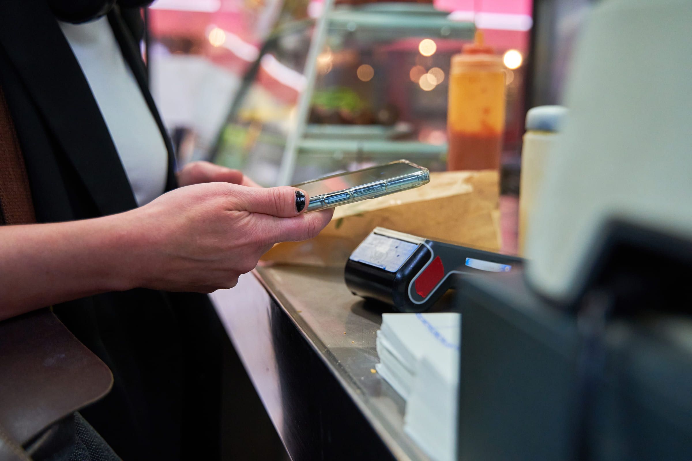 A customer paying by phone at a shop counter, card terminal in view.