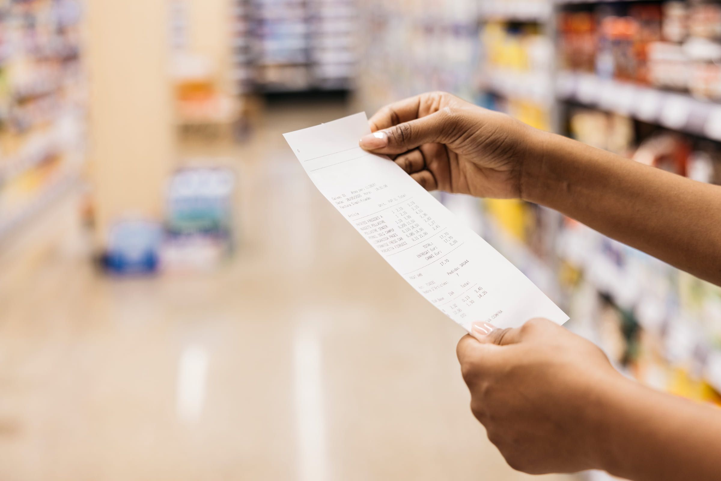 A hand holding a printed receipt in a supermarket aisle.